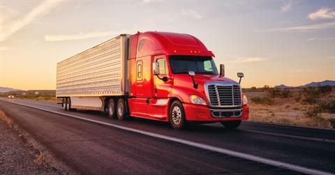 a red sixteen wheeler driving down a desert highway at sunrise