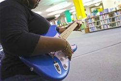 black woman playing blue electric guitar