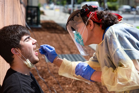 a man opening his mouth to get a throatswab covid test by a nurse in scrubs