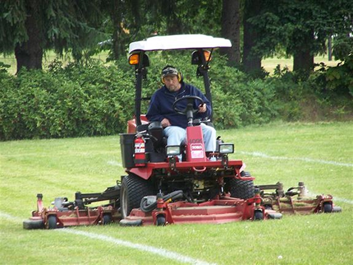 a man inside a large lawnmover drives around grass