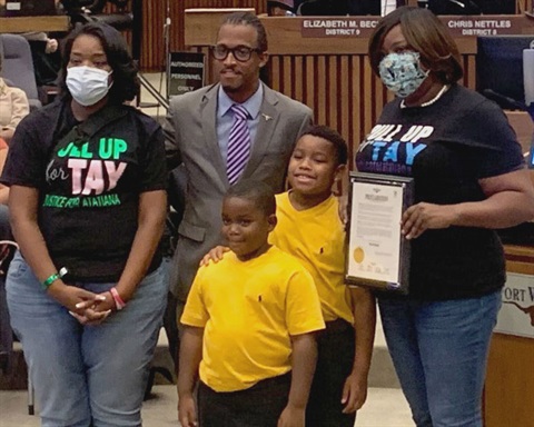 three adults and two children smile for a photo while holding up the proclamation