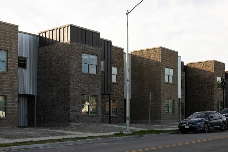 Newly built modern townhouse-style apartments along a street with parked cars.