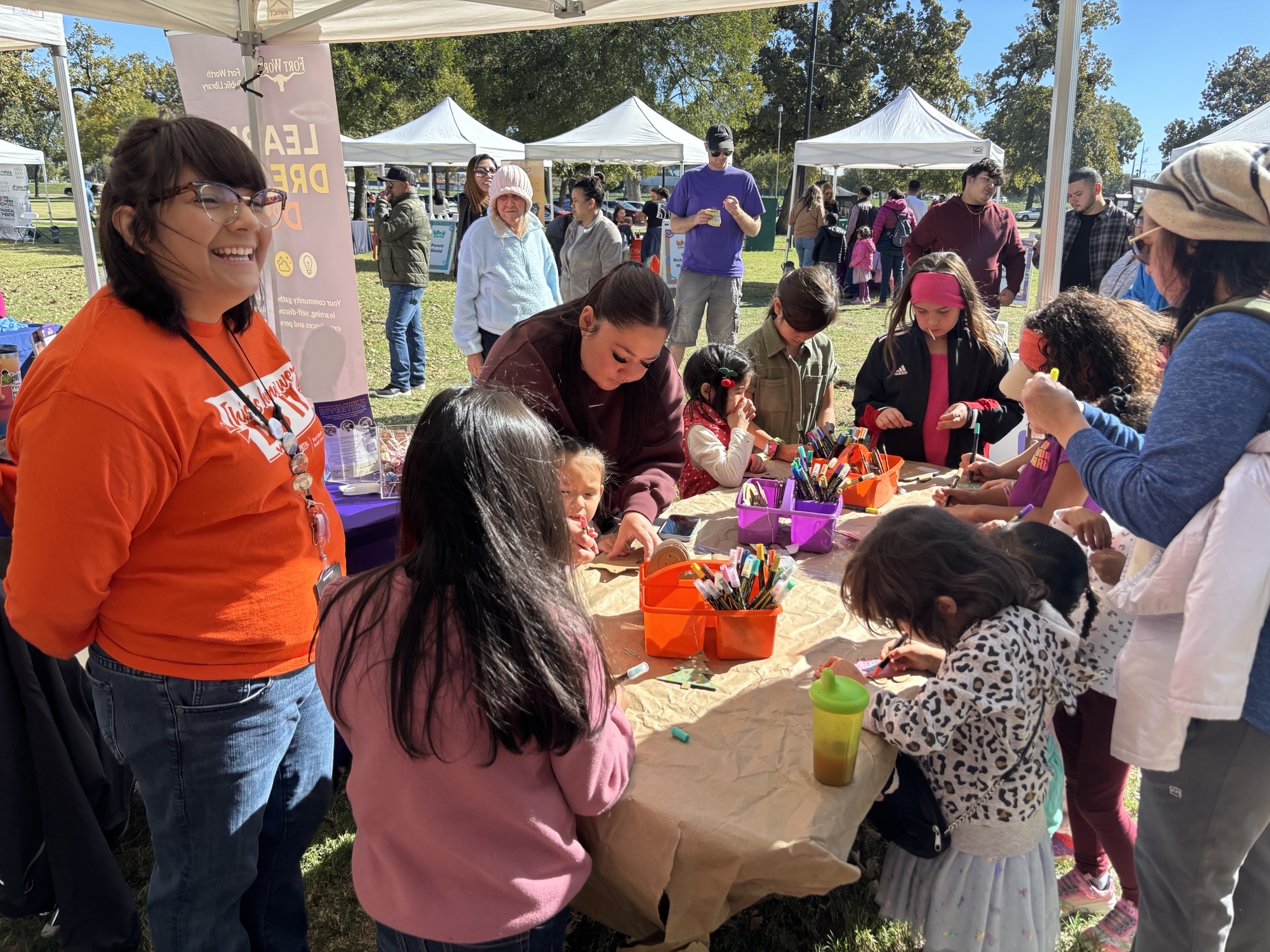 A Fort Worth Public Library Community Outreach team member stands to the left of a community outreach table.
