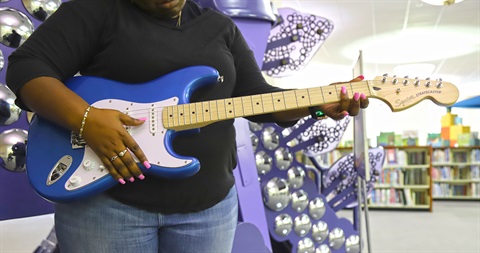 black woman playing blue electric guitar