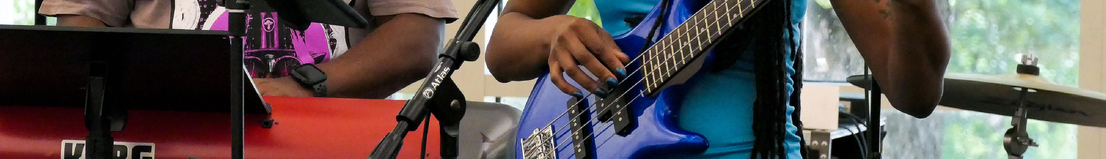 An image of two people playing instruments. The person on the left is playing keyboards and the person on the right is playing a bass guitar.