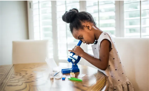 A young girl looks at things through a blue microscope.