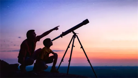photo of an adult and child with a telescope with a star-filled sky