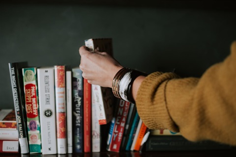 hand reaching for books on a bookshelf