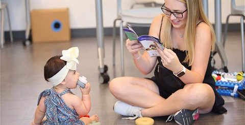 young woman reading pamphlet while baby plays