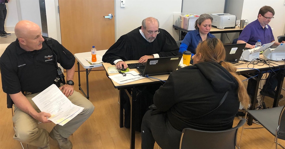 a judge and other Court employees meet at a table with a resident