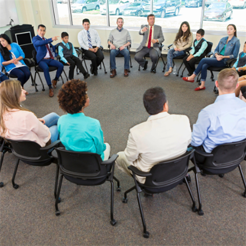 A group of people sitting in chairs in a circle having a discussion