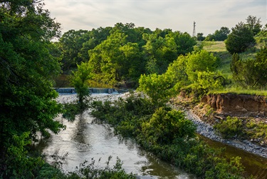 Photo of a small waterfall on Mary's creek and trees along the shore with a windmill in the background