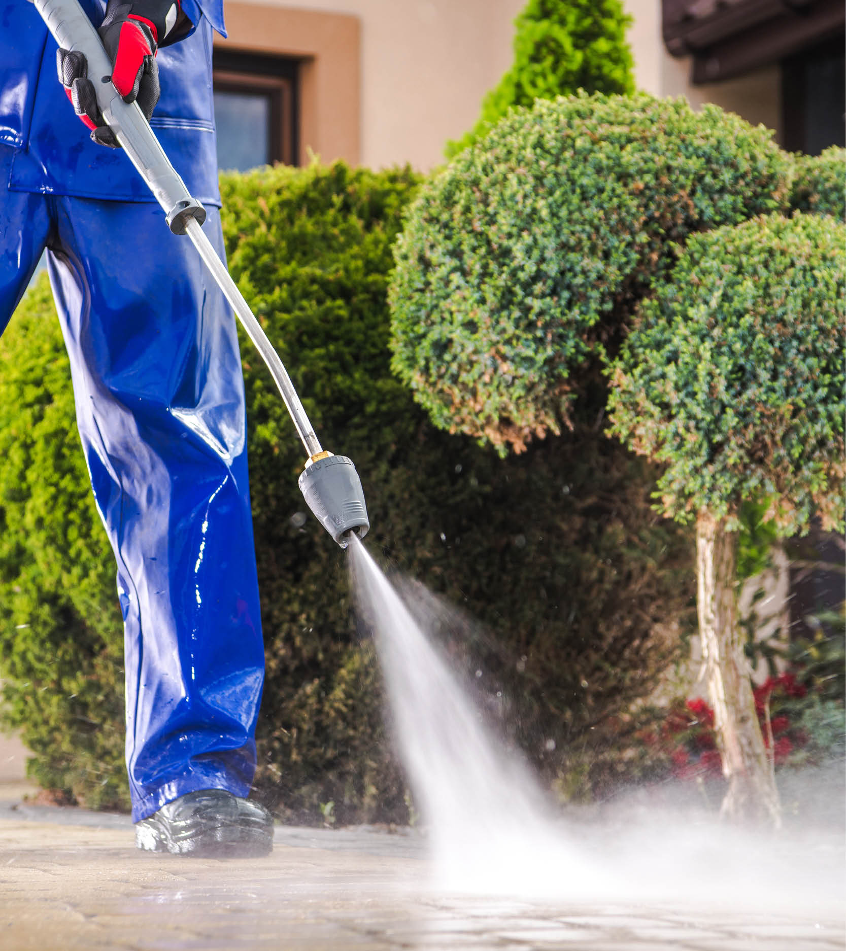 Person in protective gear using a power washer to clean an outdoor surface.
