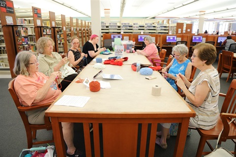 Group of women sitting at a table in the library knitting and crocheting