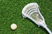 A white lacrosse stick and white lacrosse ball sit on a bed of grass.