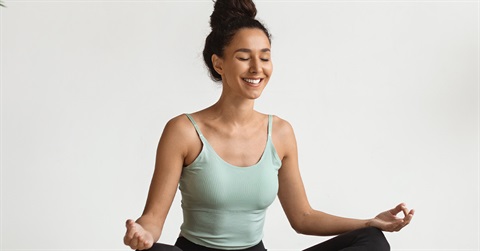 A smiling woman sits in a meditation pose
