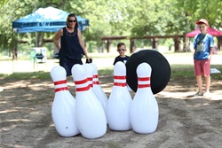 A woman and child play a game of giant bowling with blown up bowling pins and a giant bowling ball. They are outside at Trinity Park attending the Fort Worth Public Library's Summer Kickoff event.