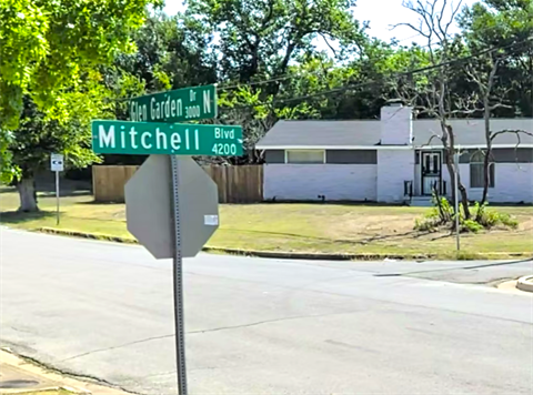 Street signs showing the intersection of Glen Garden Drive North and Mitchell Boulevard, with a one-story house, lawn, and trees in the background.
