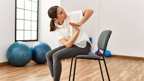 Picture of a woman performing yoga poses while sitting on a chair.
